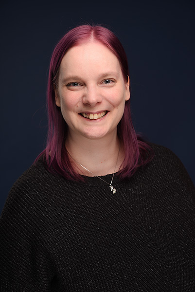 Nadine Most mit lila Haaren in einem schwarzen Strickkleid vor blauem Hintergrund